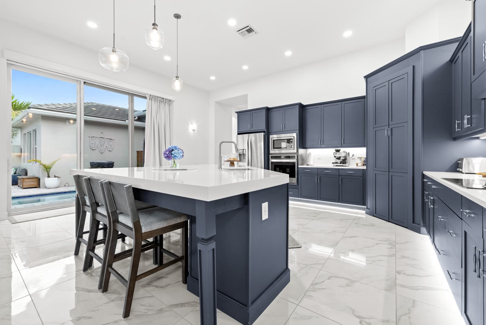 Navy blue kitchen island with pendant lighting and pool view through sliding doors