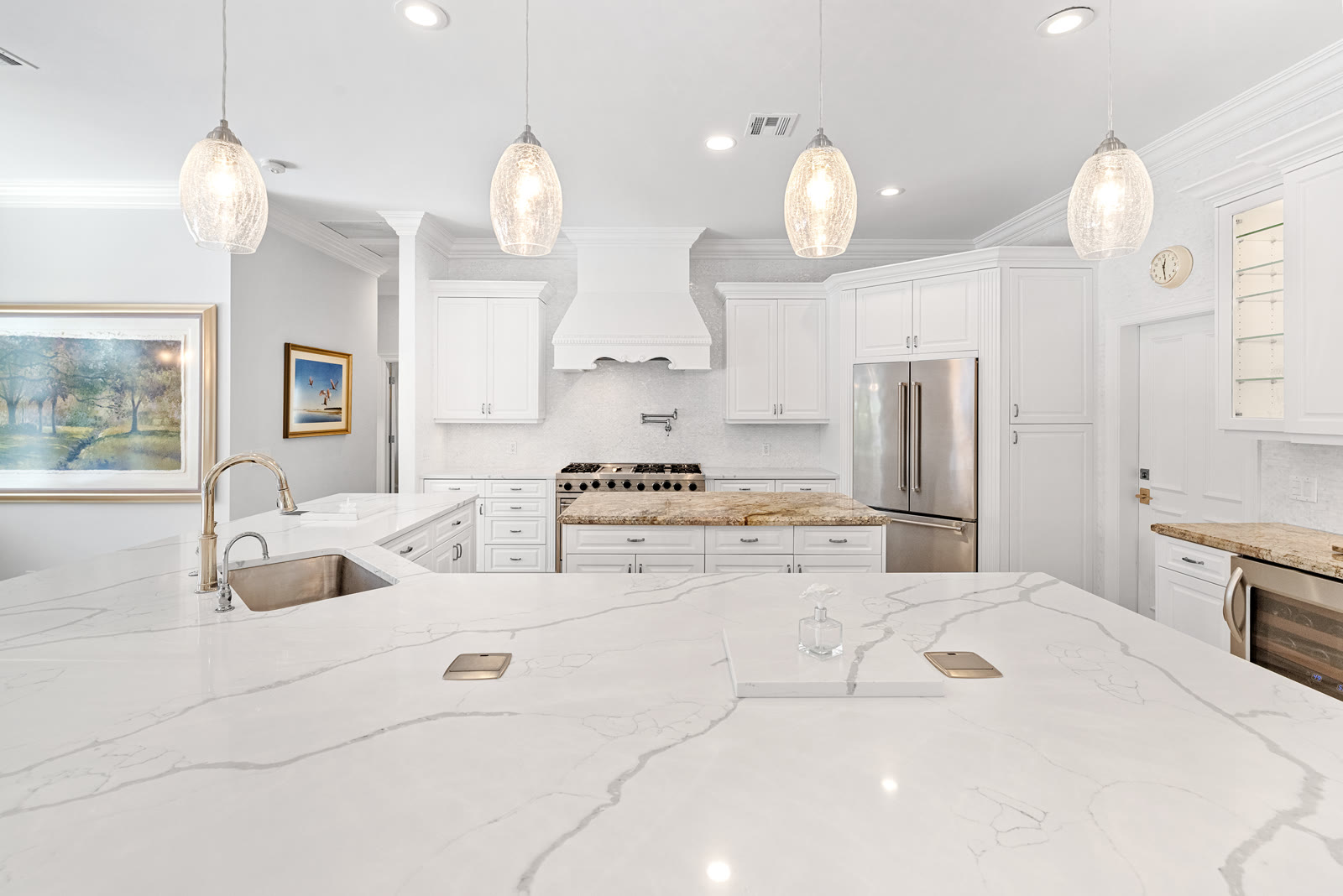 White kitchen with marble waterfall island and glass pendant lighting
